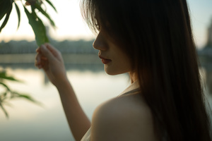 一位年轻女子手持一朵花 俯视着湖泊或河流