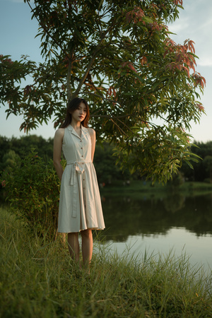 一位穿着白色连衣裙的年轻女子站在湖边或河边草地