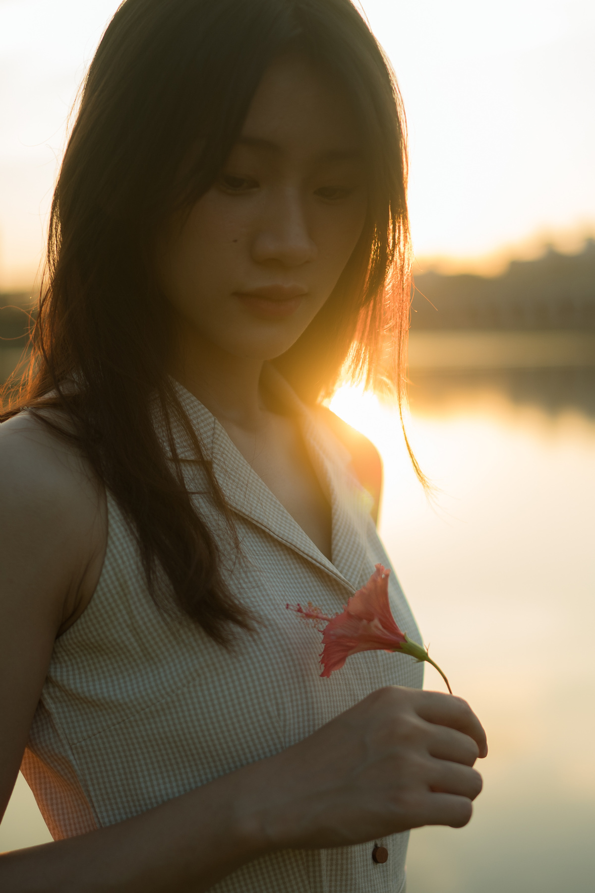 一位年轻女子手拿一束花站在日落时分的湖边 她的肖像。