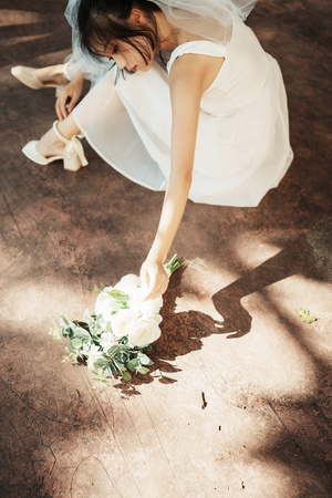 一个穿着白色连衣裙和鞋子的年轻女子 站在一束花旁边。