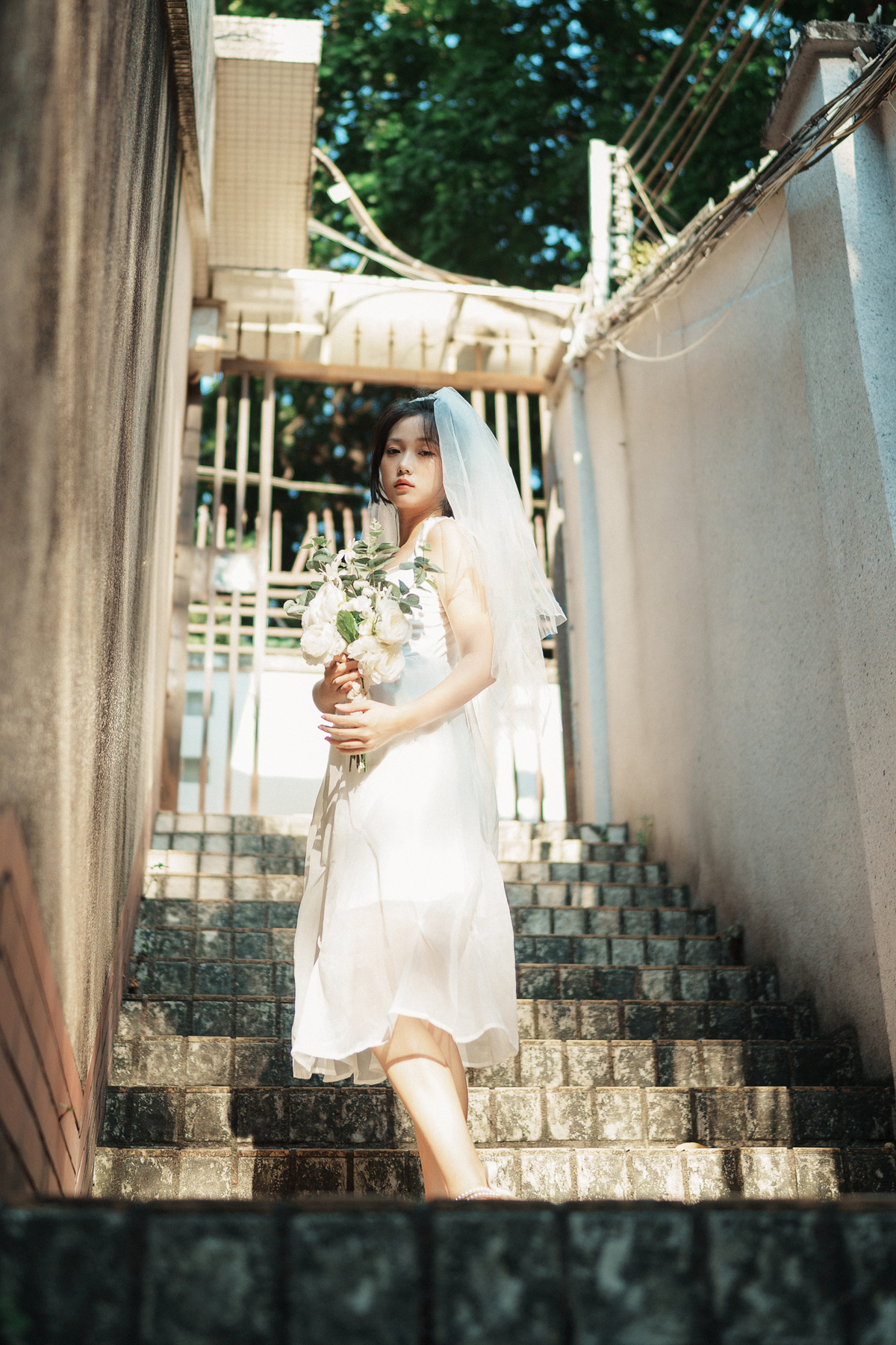 一个穿着白色连衣裙的女子手拿一束花走上楼梯