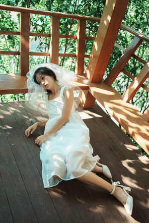 一位穿着白色连衣裙和蓝色鞋子的年轻女子坐在一棵树屋的 wooden deck 上。