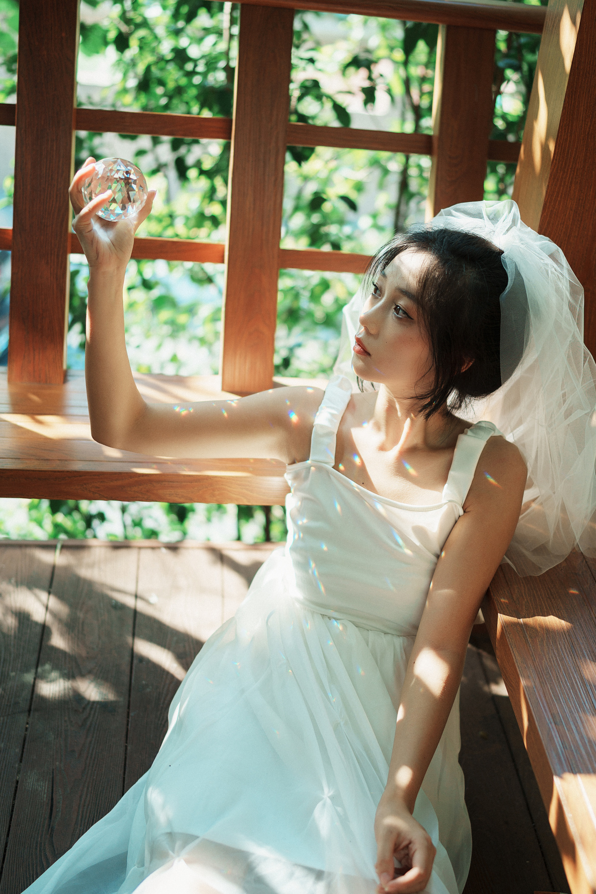 一个穿着白色连衣裙的年轻女子坐在木凳上 手里拿着一杯水。