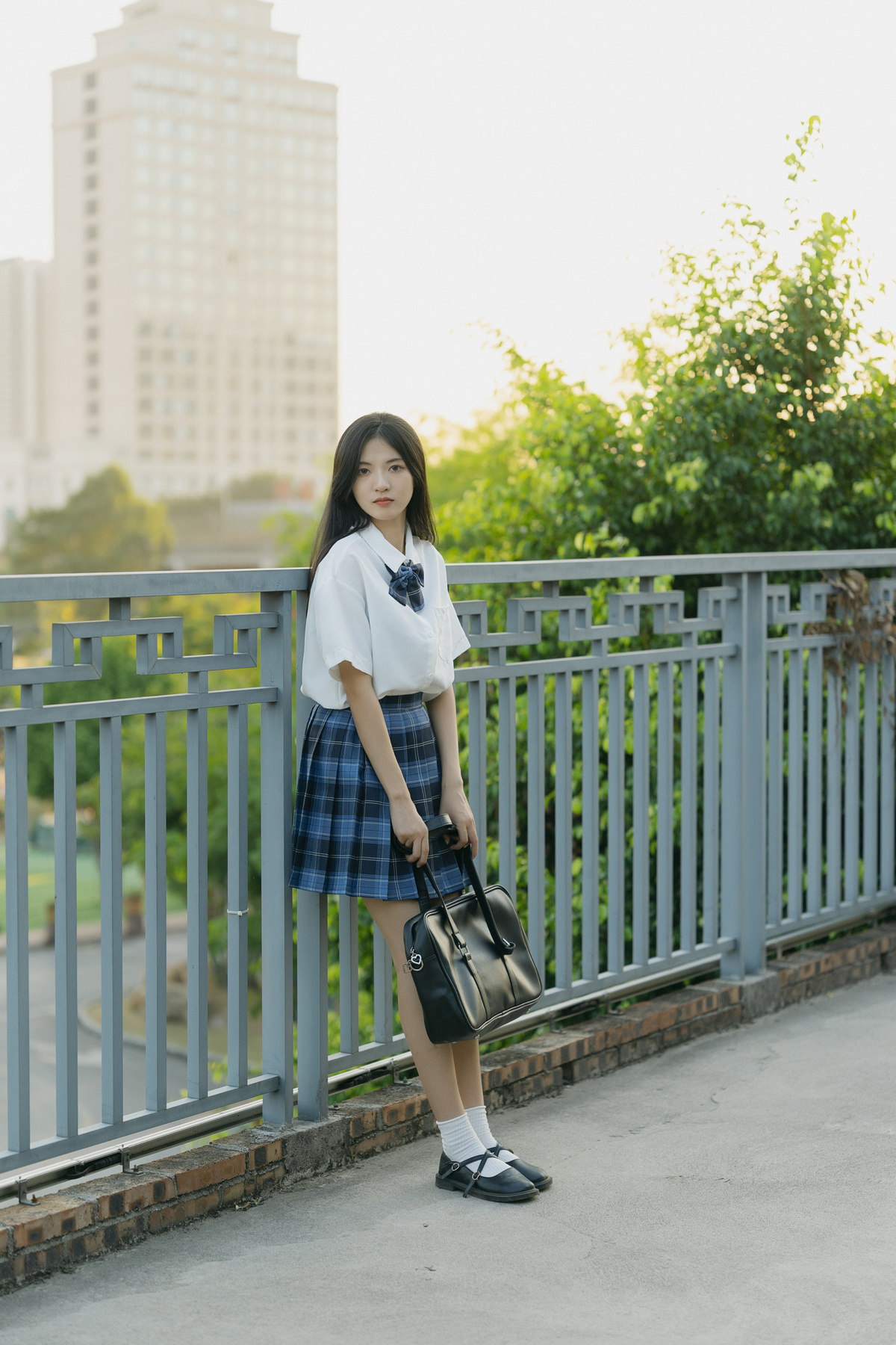 一位穿着裙子和校服的年轻女子站在桥上
