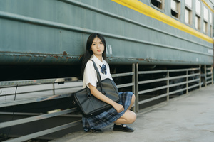 一位年轻女子背着书包和旅行箱坐在火车站。