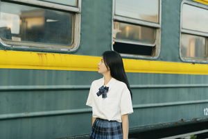 一位穿着裙子的年轻女子站在一列火车旁边