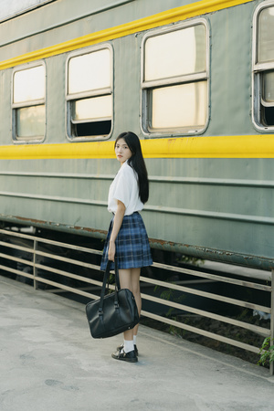 一位穿着裙子的年轻女子 carrying 一个黑色包包走向火车站