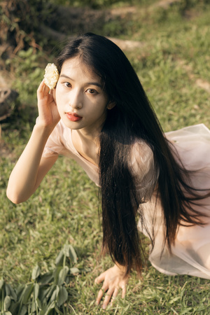 一个长发着白色裙子的年轻女子坐在田野里手里拿着一朵花