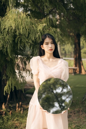 一位穿着白色连衣裙的年轻女子在公园里拿着镜子