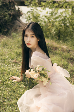 一个美丽的年轻女子穿着白色裙子坐在草地上
