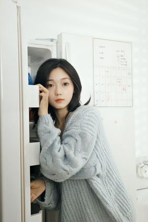 一位穿着蓝色毛衣的年轻女子站在一台打开的冰箱前