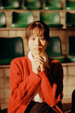 一个穿着红毛衣的年轻女子坐在椅子排里 将香烟递到嘴唇边。