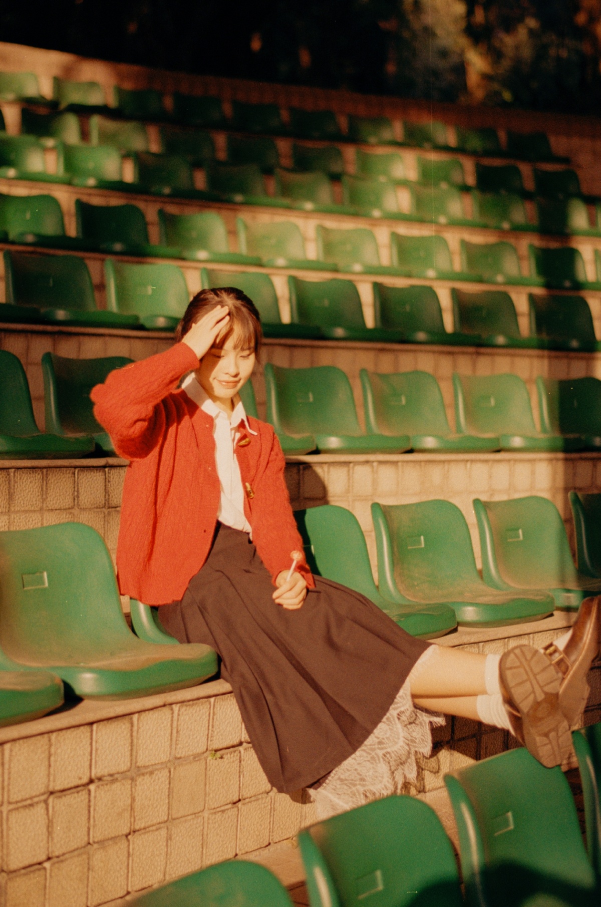 一位穿着红衣服的年轻女子坐在空荡荡的体育场里的一把绿色椅子上。