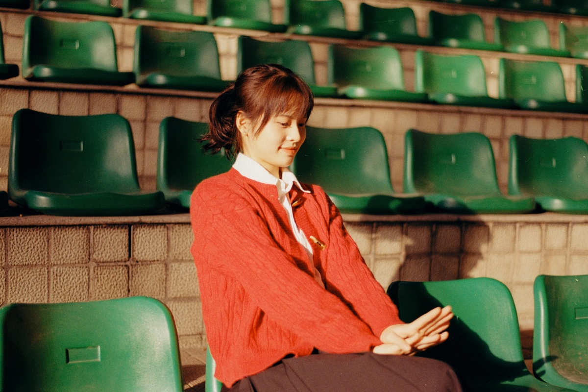 一位穿着红制服的年轻女子坐在空荡荡的体育场里 周围是绿色的椅子。