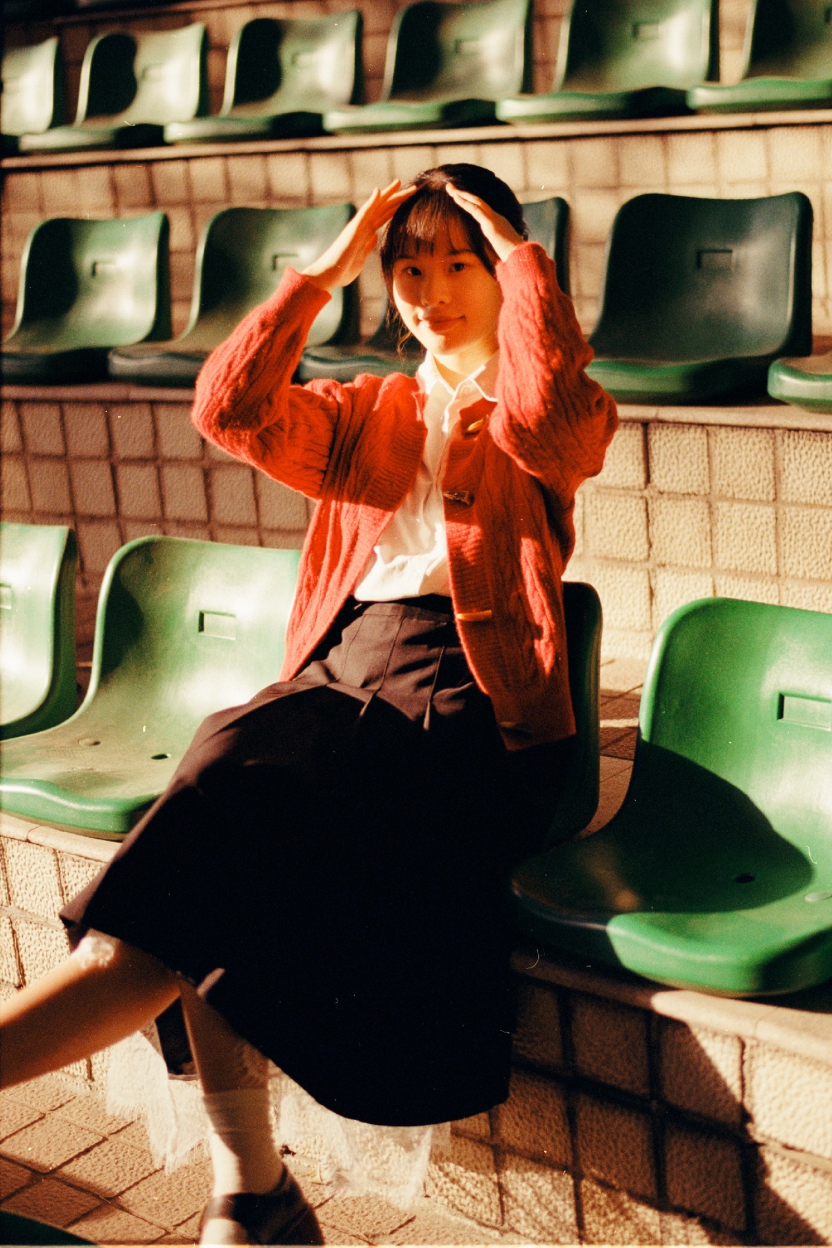 一个穿着裙子和夹克的女青年坐在绿色的椅子上 用手捂住头部