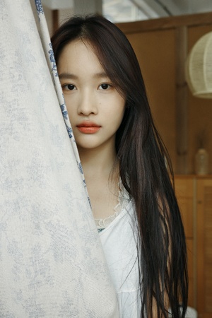 一位长发年轻女子站在白色窗帘后面