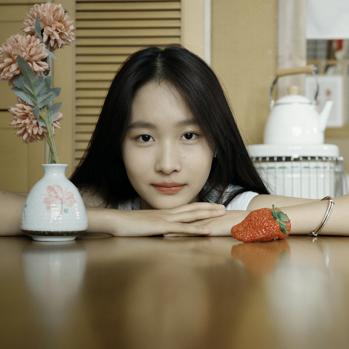 一个年轻女子坐在桌子前 双臂交叉 面前放着一束花和一株草莓。