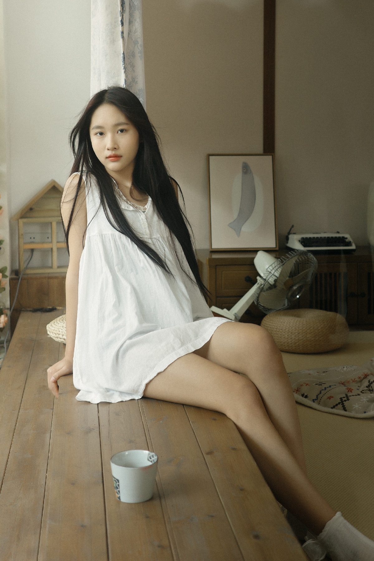 一个穿着白色连衣裙的年轻女子坐在木制桌子上的一间房间里