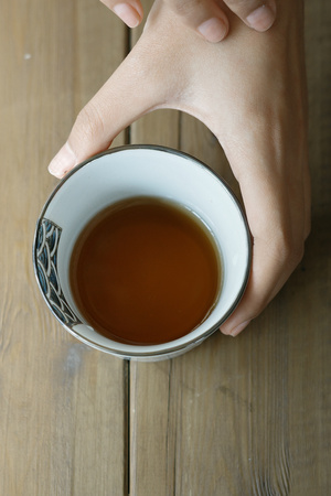 一位女子手里拿着一杯黑茶 放在木桌上。