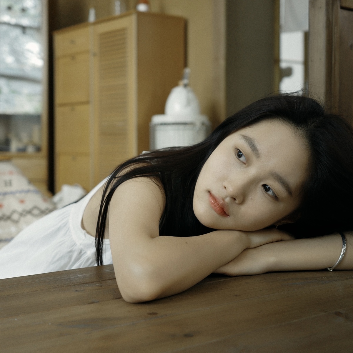 一位年轻女子躺在木制桌子上 卧室里 看着相机 另一名女子坐在床尾。
