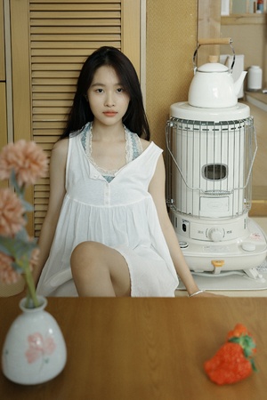 一个穿着白色连衣裙的年轻女子坐在桌子旁边 旁边有一束花。