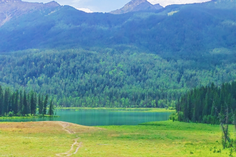 远处的山谷有树木和湖泊 前景有一条小径 远处有山脉。