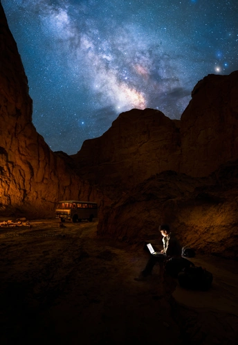 沙漠中 一男一女坐在布满星星的夜空和一座山下 手里拿着笔记本电脑