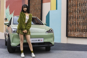 一位穿着绿色外套的年轻女子站在街上的一辆汽车旁边