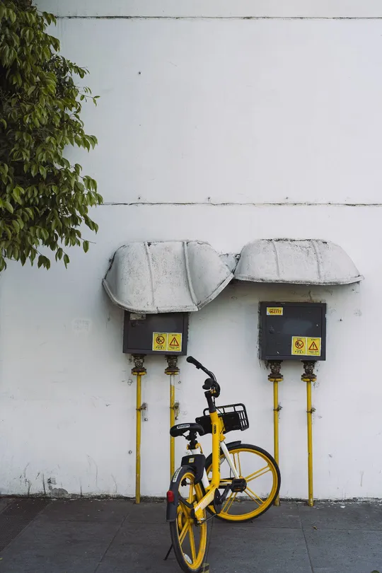 一辆黄色的自行车停在白色建筑前 车前有一个倾斜的停车计时器靠在墙上。