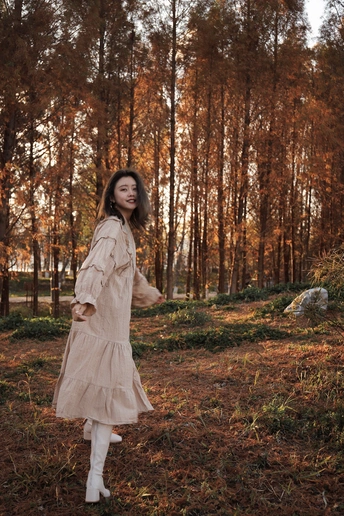 一个穿着白色连衣裙和靴子的年轻女子穿过树林