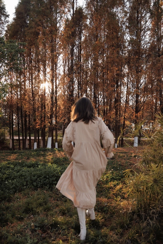一位身穿白色连衣裙、打着雨伞的年轻女子穿过一片树林