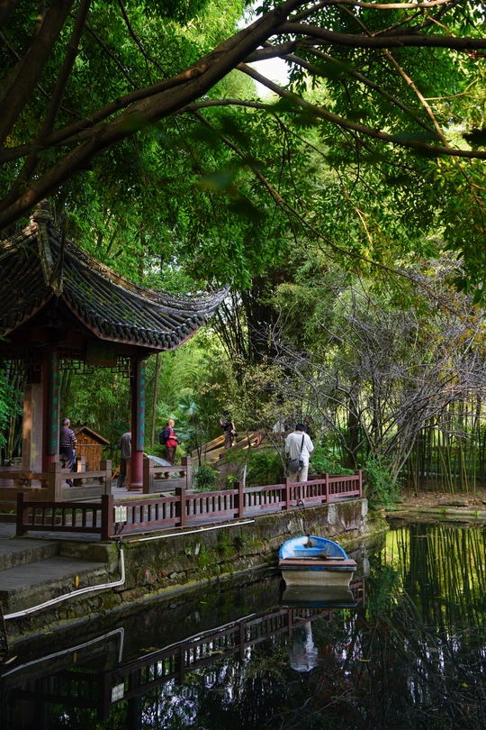 一个小池塘里有一艘小船和水上的人 以及一座桥上的人们。