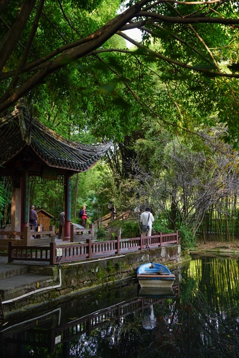 一个小池塘里有一艘小船和水上的人 以及一座桥上的人们。