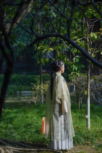 一位穿着连衣裙 手持雨伞的年轻女子走在森林小径上 周围有树木和草地。