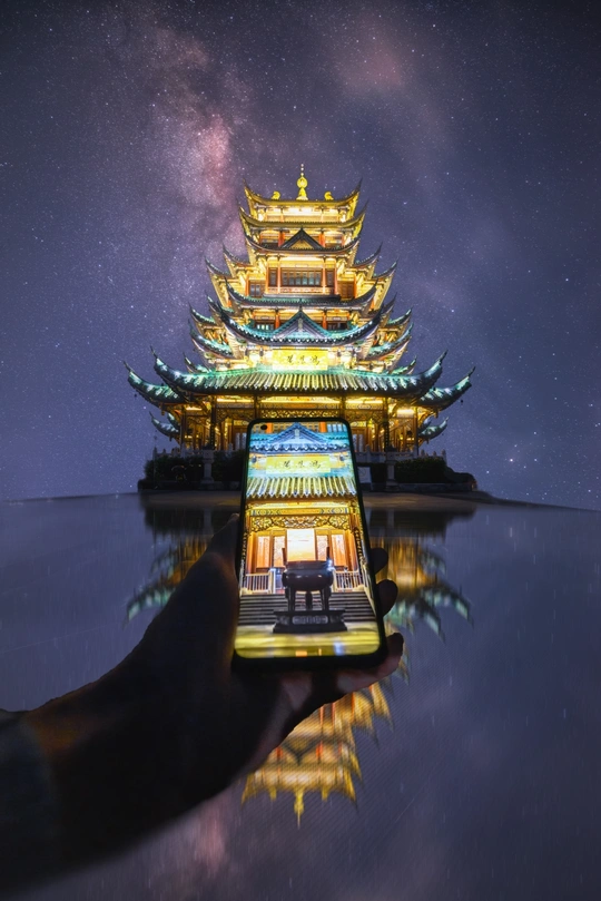一个人手里拿着智能手机 在夜晚拍摄日本风格城堡 背景是星空。