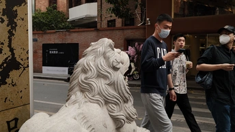 一个戴面具的人在人行道上站在一尊白狮子雕像旁边 人们路过。