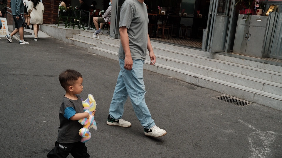 一个年轻男子用手抱着一个小男孩走在人行道上 同时一个男子用手抱着一个小孩走在人行道上。