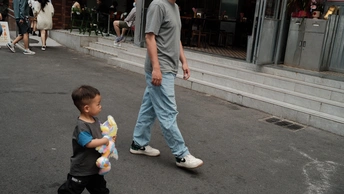 一个年轻男子用手抱着一个小男孩走在人行道上 同时一个男子用手抱着一个小孩走在人行道上。