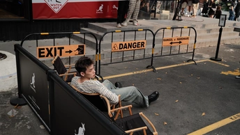 一个年轻男子坐在街边的一把椅子上 背景有人在活动。