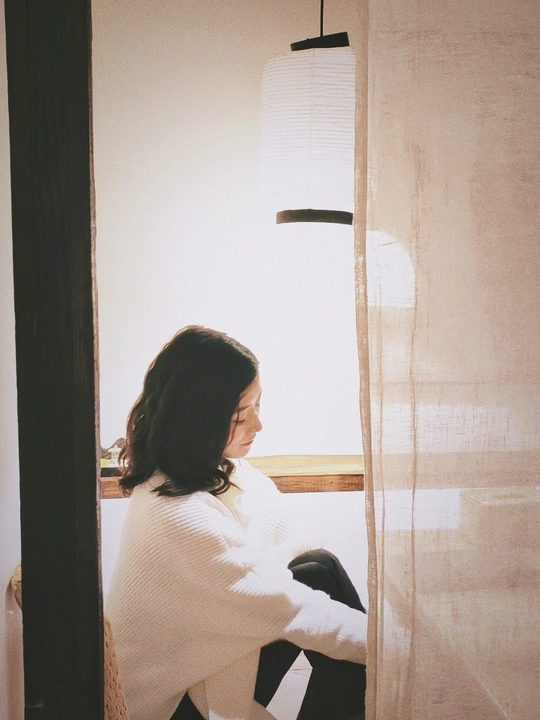 一个坐在窗户边的白色椅子旁边的女人