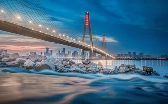 夕阳下跨越河流的吊桥 背景是一座城市。