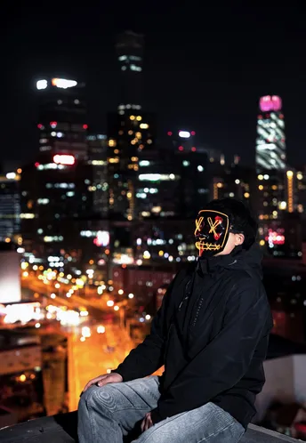 戴面具遮住脸和眼睛的男人坐在俯瞰城市的阳台上。