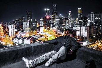 一个男人坐在屋顶的围墙上 俯瞰着夜晚的城市。