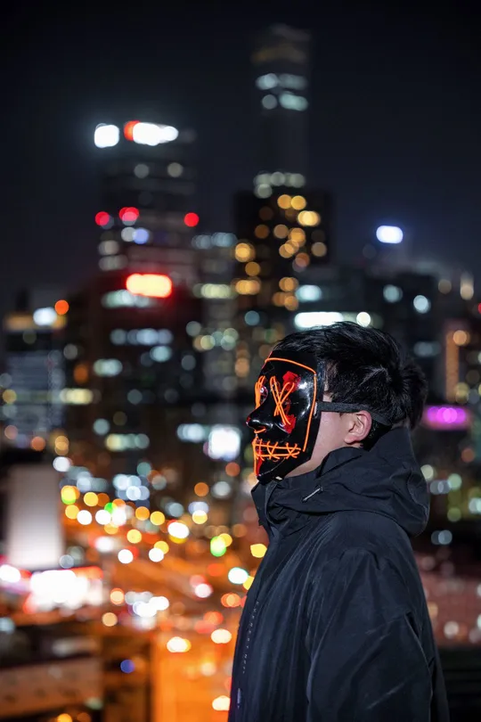 一个戴面具的男子站在屋顶上 晚上看着城市