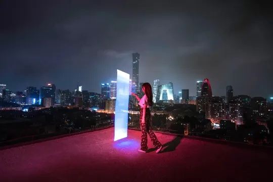 一个男子和一个女子站在屋顶露台 夜晚有红光 俯瞰城市天际线。