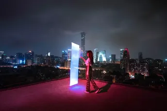 一个男子和一个女子站在屋顶露台 夜晚有红光 俯瞰城市天际线。