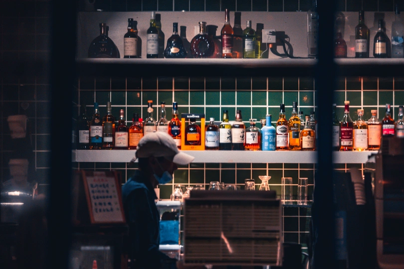 一个人站在厨房里 透过窗户看着一家酒吧 货架上摆着几瓶酒