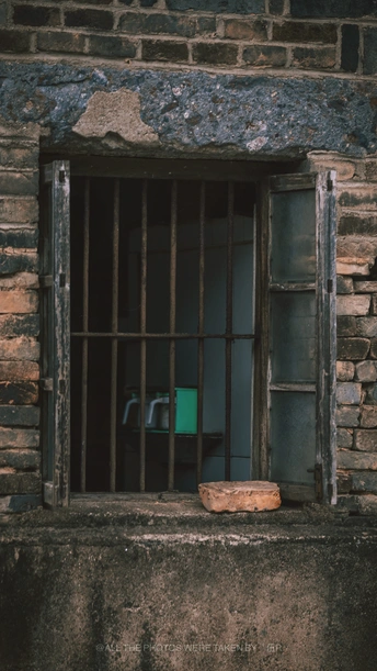 一座古老的砖砌建筑 窗户上有栏杆 窗台上的桌子旁有一把椅子