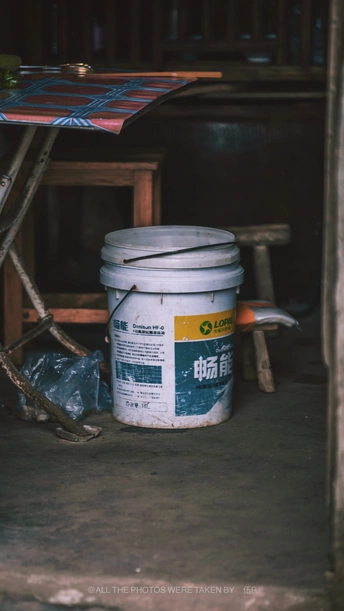 一个放在伞下的白色水桶 旁边是一张木桌