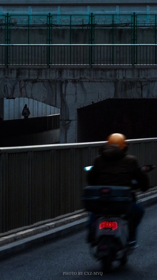 一个人在夜晚骑摩托车在人行桥附近的道路上 有一个男人在驾驶摩托车。